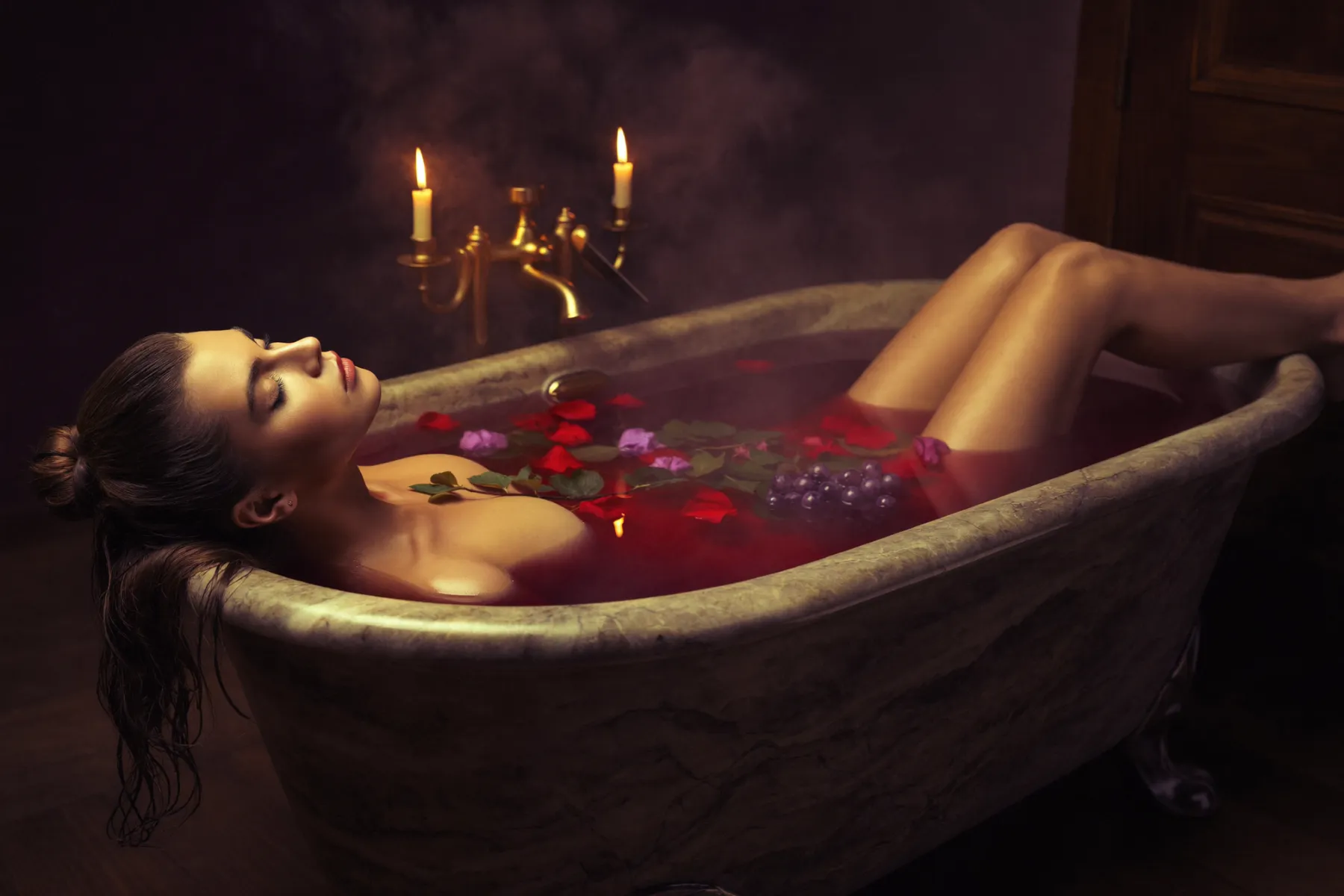 Femme allongée dans un bain de vin grenat, ambiance de spa tamisée aux chandelles