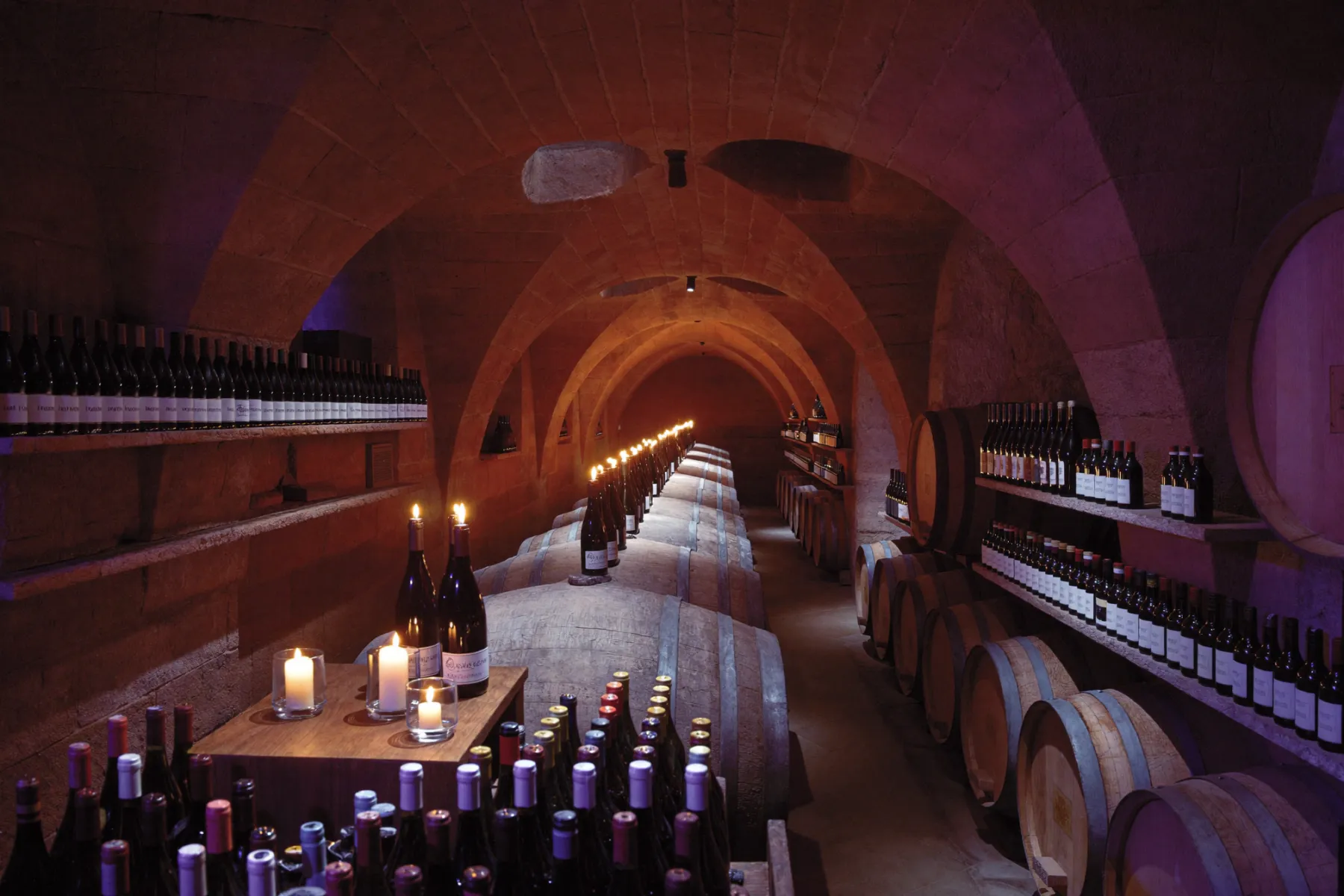 Ambiance tamisée aux chandelles autour du vin, bouteilles et tonneaux