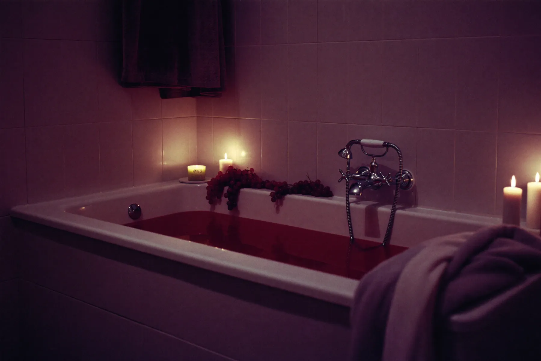 Salle de bain transformée en spa, eau grenat, raisins et bougies au bord de la baignoire