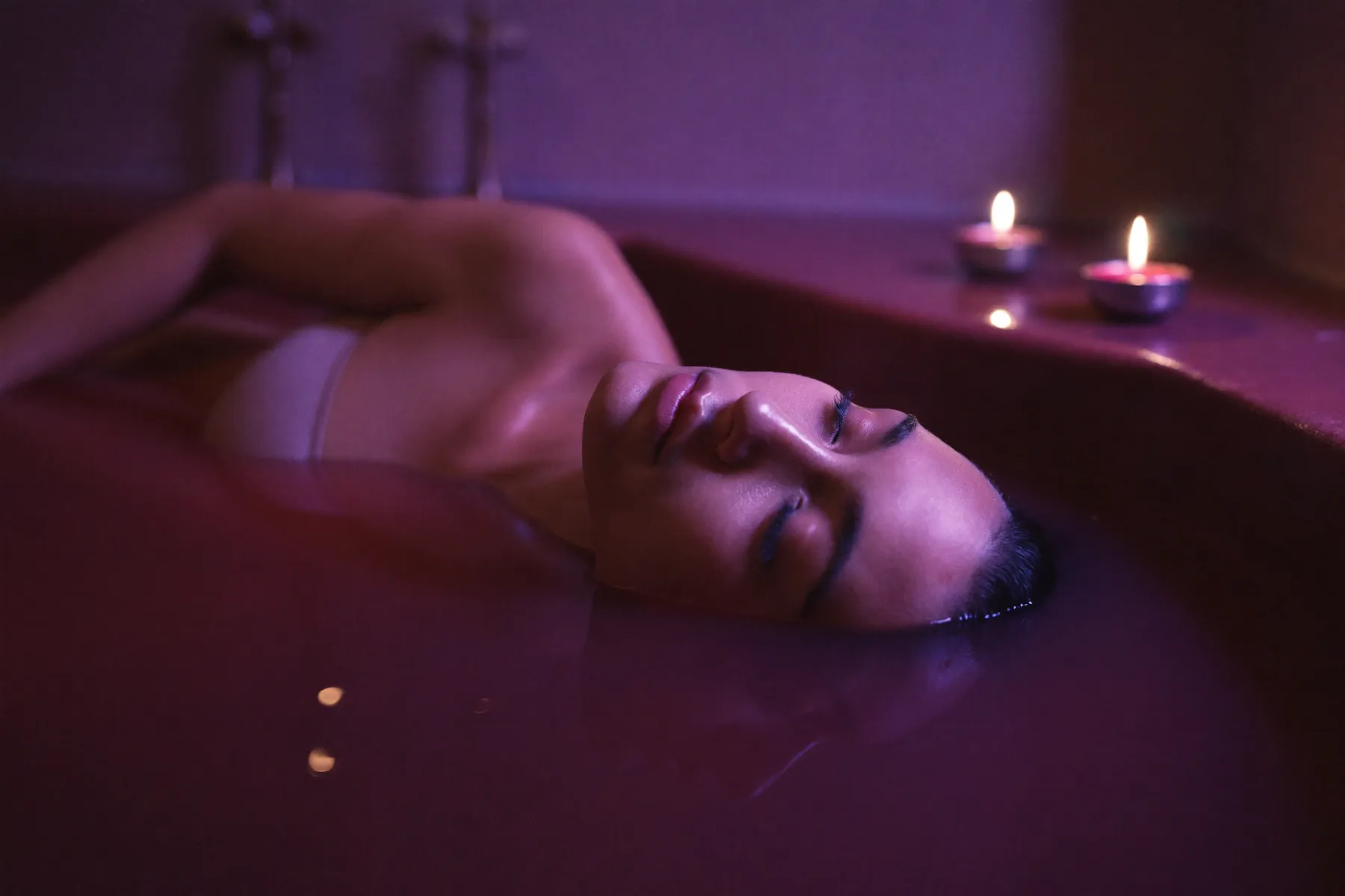 Femme sereine se reposant dans un bain de vin grenat aux chandelles